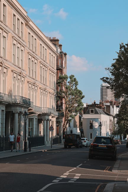 A residential street in Kentish Town NW5 featuring a row of historic Victorian-style buildings with cream-colored facades, decorative iron balconies, and large sash windows. The street is paved with a